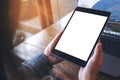 Mockup image of hands holding black tablet pc with white blank screen and laptop on wooden table background Royalty Free Stock Photo