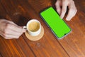 Mockup image of hands holding mobile phone with blank green screen with coffee cup on wooden table. Top view Royalty Free Stock Photo