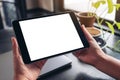 Hands holding and using black tablet pc with blank white desktop screen with notebook, green leaves and coffee cup on wooden table Royalty Free Stock Photo