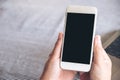 Mockup image of hands holding white mobile phone with blank black desktop screen and laptop