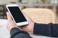 A hands holding white mobile phone with blank black desktop screen on table in modern cafe Royalty Free Stock Photo