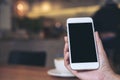 Hands holding white mobile phone with blank black screen with coffee cups on wooden table in restaurant Royalty Free Stock Photo