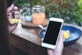 Mockup image of hands holding white mobile phone with blank black screen while eating yellow lemon curd cake on wooden table Royalty Free Stock Photo