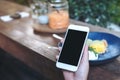 Mockup image of hands holding white mobile phone with blank black screen while eating yellow lemon curd cake on wooden table Royalty Free Stock Photo