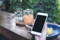 Mockup image of hands holding white mobile phone with blank black screen while eating yellow lemon curd cake on wooden table Royalty Free Stock Photo