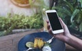 Mockup image of hands holding white mobile phone with blank black screen while eating yellow lemon curd cake on wooden table Royalty Free Stock Photo