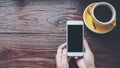 Mockup image of hands holding white mobile phone with blank black screen with yellow hot coffee cups on vintage wooden table Royalty Free Stock Photo