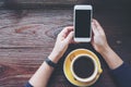 Mockup image of hands holding white mobile phone with blank black screen with yellow hot coffee cups on vintage wooden table Royalty Free Stock Photo