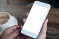 Hands holding white mobile phone with blank desktop screen with coffee cup on wooden table in cafe Royalty Free Stock Photo