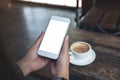 Hands holding white mobile phone with blank desktop screen with coffee cup on wooden table in cafe Royalty Free Stock Photo