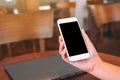 Hands holding white mobile phone with blank desktop screen with laptop computer on the table Royalty Free Stock Photo