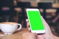 Hands holding white mobile phone with blank green screen with coffee cups on wooden table in restaurant Royalty Free Stock Photo