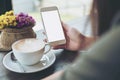 Hands holding white mobile phone with blank white screen with hot coffee cup and flower vase in cafe Royalty Free Stock Photo