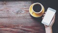 Mockup image of hands holding white mobile phone with blank screen with yellow hot coffee cups on vintage wooden table Royalty Free Stock Photo