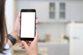 Mockup image of hands showing black mobile phone with blank white screen on blur kitchen background. Royalty Free Stock Photo
