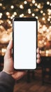 Mockup image of a man& x27;s hand holding black mobile phone with blank white screen over blurred christmas lights Royalty Free Stock Photo