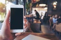 Mockup image of a man`s hand holding and raising a white mobile phone with blank black screen in cafe Royalty Free Stock Photo