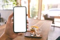 A man`s hand holding and showing black mobile phone with blank white screen while sitting in cafe Royalty Free Stock Photo