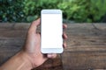 Mockup image of a man`s hand holding and using white smart phone with blank screen on wooden table and green nature Royalty Free Stock Photo