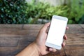 Mockup image of a man`s hand holding and using white smart phone with blank screen on wooden table and green nature Royalty Free Stock Photo