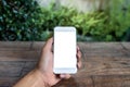 Mockup image of a man`s hand holding and using white smart phone with blank screen on wooden table and green nature Royalty Free Stock Photo