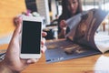 Mockup image of a man`s hand holding white mobile phone with blank black screen in modern cafe and blur woman reading newspaper Royalty Free Stock Photo