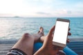 Mockup image of a man`s hand holding white mobile phone with blank desktop screen sitting by the sea and blue sky Royalty Free Stock Photo