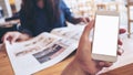 Mockup image of a man`s hand holding white mobile phone with blank screen in modern cafe and blur woman reading newspaper Royalty Free Stock Photo