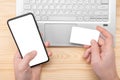 Mockup image. Online Shopping And E-Payments. man hands hold cell phone with blank white screen and mockup credit card on lapto Royalty Free Stock Photo