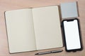 Mockup image of a smartphone with the blank white screen, pen, sticky notes and a notebook on a wooden table. Royalty Free Stock Photo