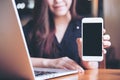 Mockup image of a smiley Asian beautiful woman holding and showing white mobile phone with blank black screen while using laptop