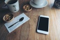 Mockup image of white mobile phone with blank black screen , coffee cups and snacks on vintage wooden table