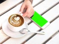 Mockup image of white mobile phone with blank black screen and hand holding hot latte coffee on vintage wood table in Royalty Free Stock Photo