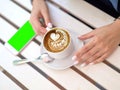 Mockup image of white mobile phone with blank black screen and hand holding hot latte coffee on vintage wood table in Royalty Free Stock Photo
