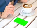 Mockup image of white mobile phone with blank black screen and hand holding hot latte coffee on vintage wood table in Royalty Free Stock Photo