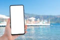 Mockup image of a woman hand holding cell mobile phone with blank desktop screen by the sea and blue sky Royalty Free Stock Photo
