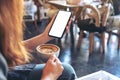 A woman holding black mobile phone with blank screen while drinking coffee in vintage cafe