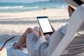 A woman holding a black tablet pc with blank desktop screen while laying down on beach chair on the beach Royalty Free Stock Photo