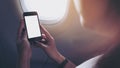 Mockup image of a woman holding and looking at black smart phone with black white screen next to an airplane window Royalty Free Stock Photo