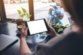 A woman holding and looking at black tablet pc with blank white desktop screen with notebook, green leaves and coffee cup on woode Royalty Free Stock Photo