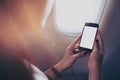 A woman holding and looking at smart phone with blank white screen next to an airplane window with clouds and sky background Royalty Free Stock Photo