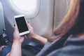 Mockup image of a woman holding and looking at white smart phone with blank black desktop screen next to an airplane window Royalty Free Stock Photo
