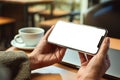 A woman holding mobile phone with blank white desktop screen with laptop and coffee cup on table Royalty Free Stock Photo