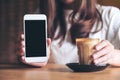 A woman holding and showing white mobile phone with blank black desktop screen with coffee cup on wooden table Royalty Free Stock Photo