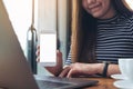 A woman holding and showing white mobile phone with blank screen on the table while using laptop Royalty Free Stock Photo