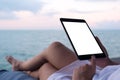 A woman holding and using black tablet with blank white desktop screen while sitting by the sea with blue sky background Royalty Free Stock Photo