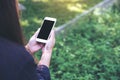 Mockup image of a woman holding and using white smart phone with blank black desktop screen in outdoor with green nature Royalty Free Stock Photo