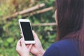 Mockup image of a woman holding and using white smart phone with blank black screen in outdoor and green nature Royalty Free Stock Photo