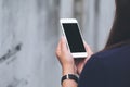 Mockup image of a woman holding and using white smart phone with blank black screen in outdoor and old white concrete wall Royalty Free Stock Photo