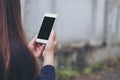 Mockup image of a woman holding and using white smart phone with blank black screen in outdoor and old white concrete wall Royalty Free Stock Photo